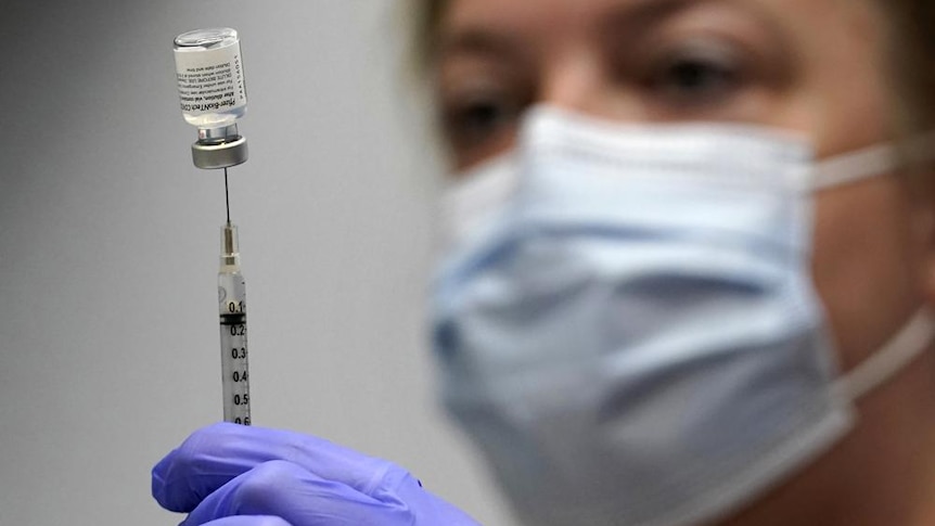 A woman holds a syringe that is stuck into an upside down vial