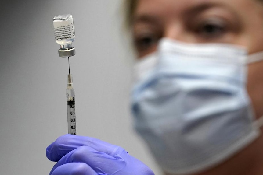 A woman holds a syringe that is stuck into an upside down vial