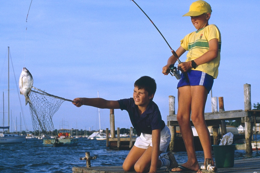 Two young boys fishing on a pier.