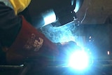 A man welds a piece of metal while wearing a welding mask.
