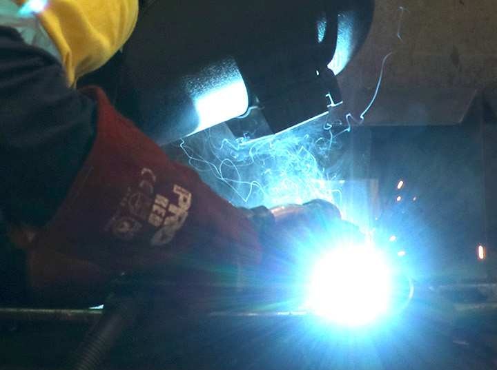 A man welds a piece of metal while wearing a welding mask.