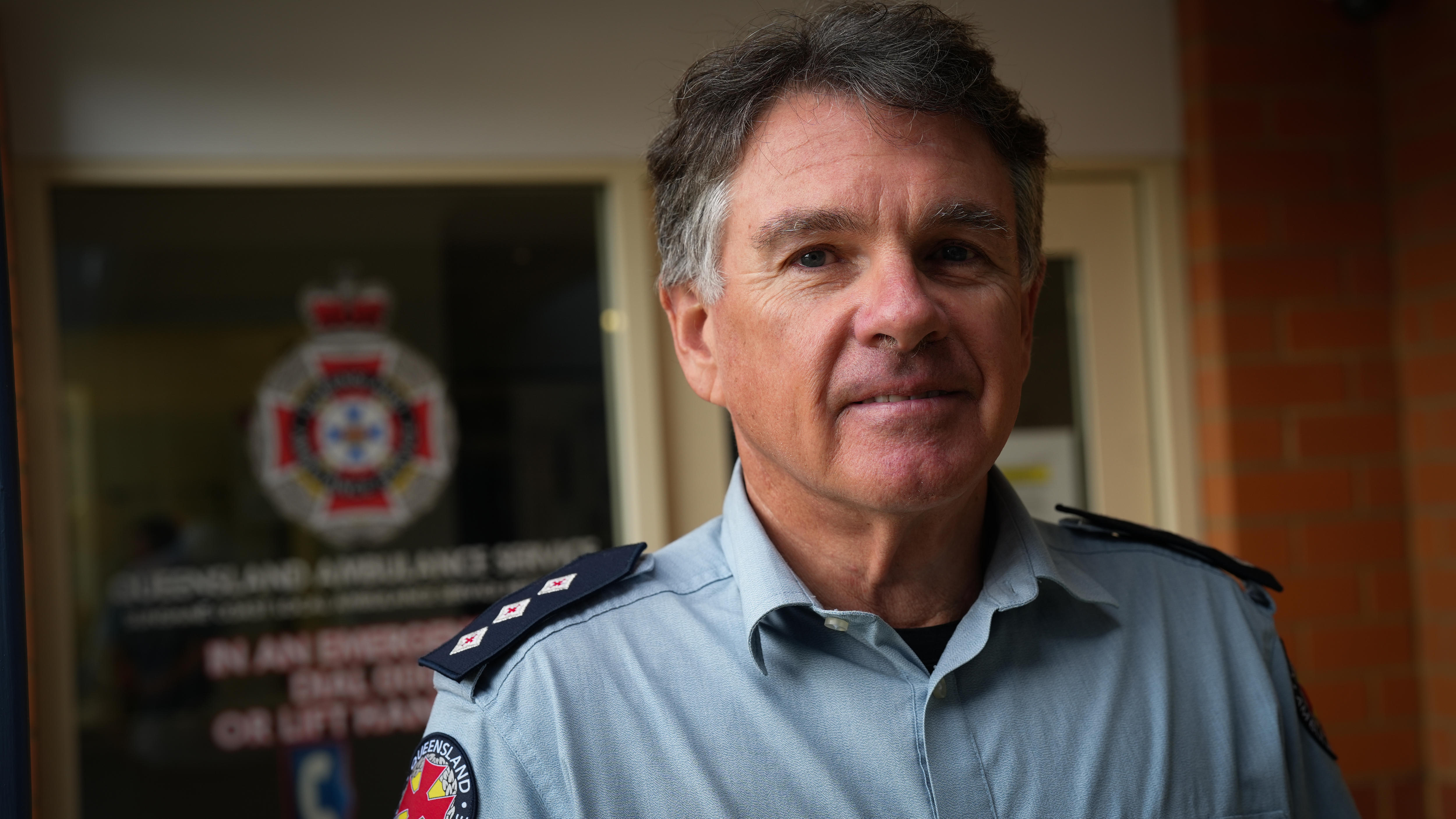 A a man in his fifties in an ambulance uniform looks at the camera.
