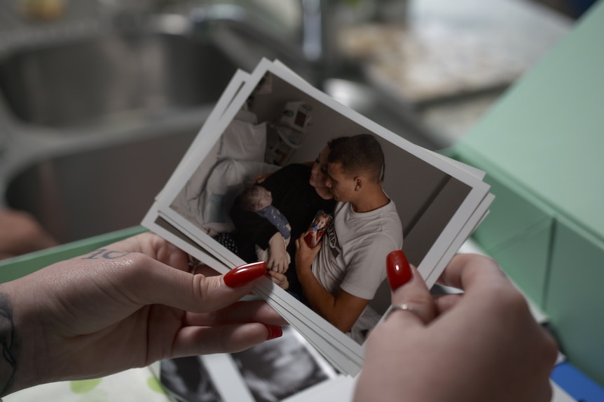 A woman's hands holds a photo of a man and woman holding a baby.