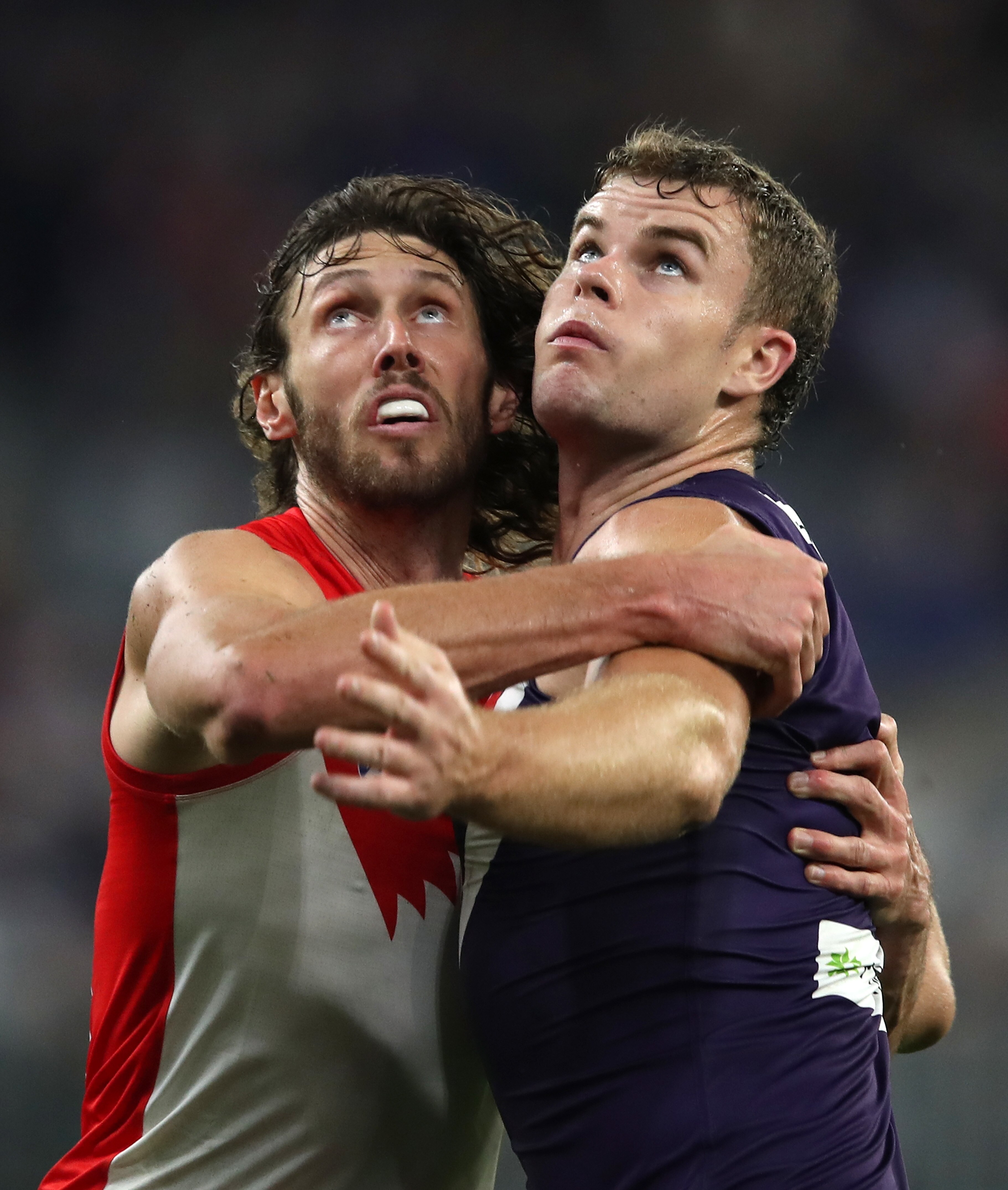 A Sydney Swans AFL player pushes against a Fremantle opponent as they both look at the ball in the air.