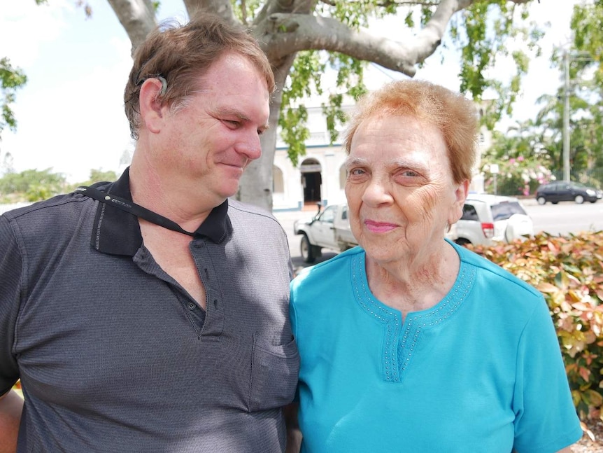 A man with a visible cochlear implant stares at his mother while his mother stares into the camera.