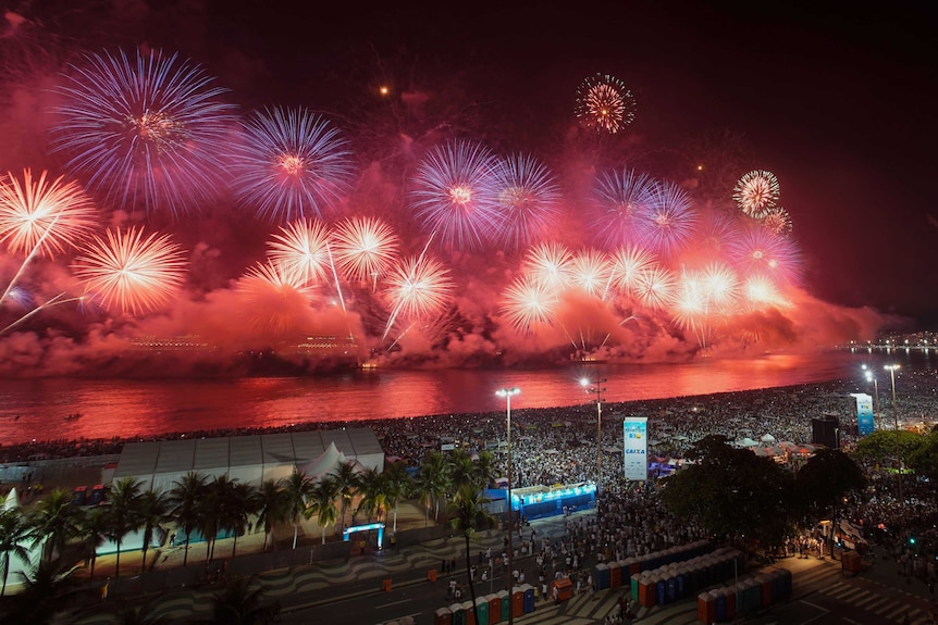 Fireworks explode in red and purple along over the waterfront of Copacabana Beach.