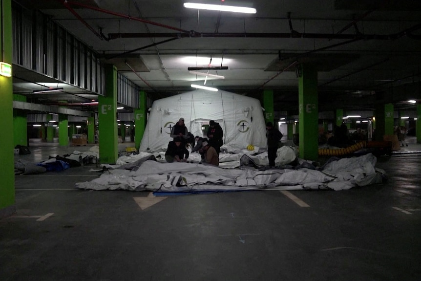 People in an underground parking garage, setting up a field hospital 