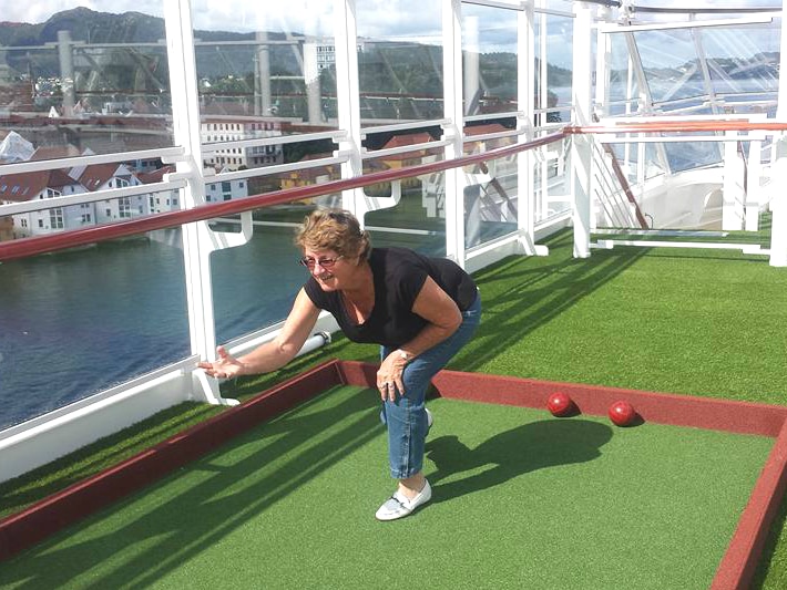 Woman playing lawn bowls on what looks like a cruise ship.