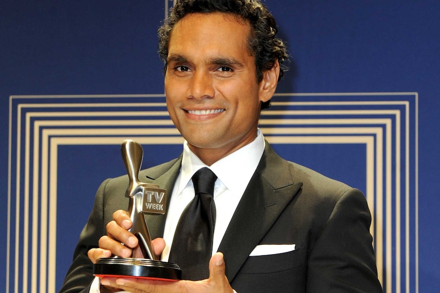 Rob Collins holds his silver logie holding a black suit and tie backstage