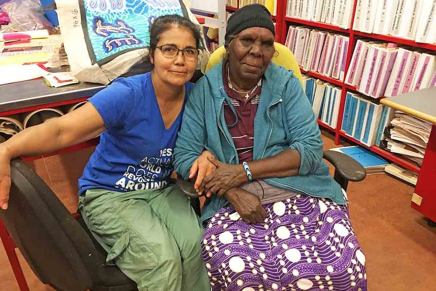 Two women sitting on a couch arm in arm.