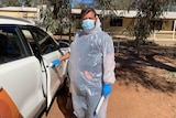 A man in personal protective equipment stands next to his car in Wilcannia. 
