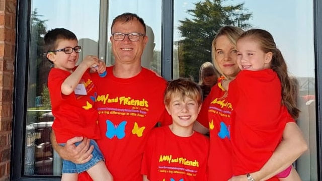 Family of five standing together wearing matching red shirts with a Cockayne Syndrome logo on the front.