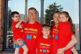Family of five standing together wearing matching red shirts with a Cockayne Syndrome logo on the front.