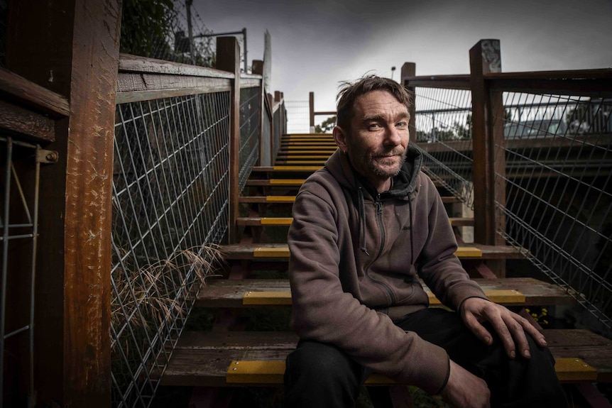 A middle aged man sitting on stairs looking at the camera