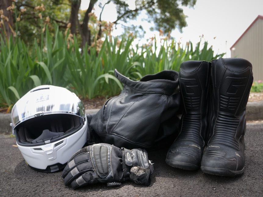 A white motorbike helmet, gloves, leather jacket and riding boots on the ground. Photo taken November 2021.