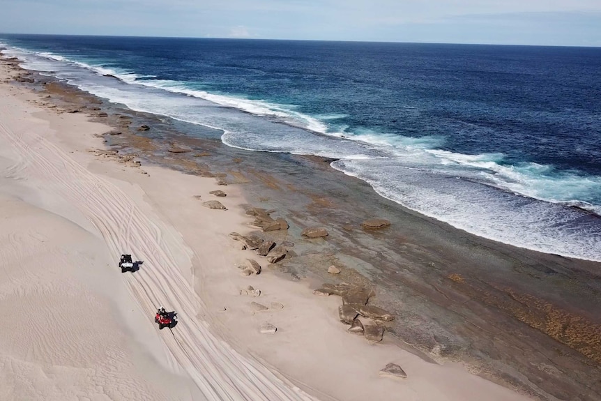 Two quad bikes driving along a vast stretch of empty beach.