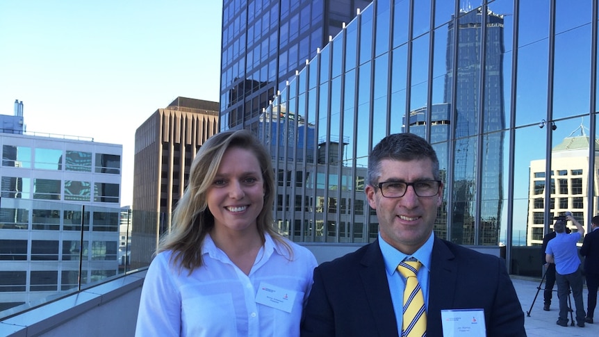 Emma Sutherland and Jim Riordan pose on a high rise balcony in front of towering office buildings