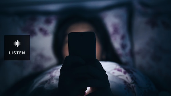 Image of a woman in bed at night scrolling on her phone. . Has Audio.