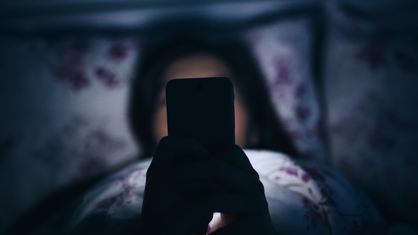 Image of a woman in bed at night scrolling on her phone. 