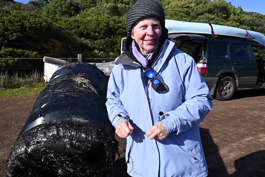 A woman stands next to a large, black cylinder