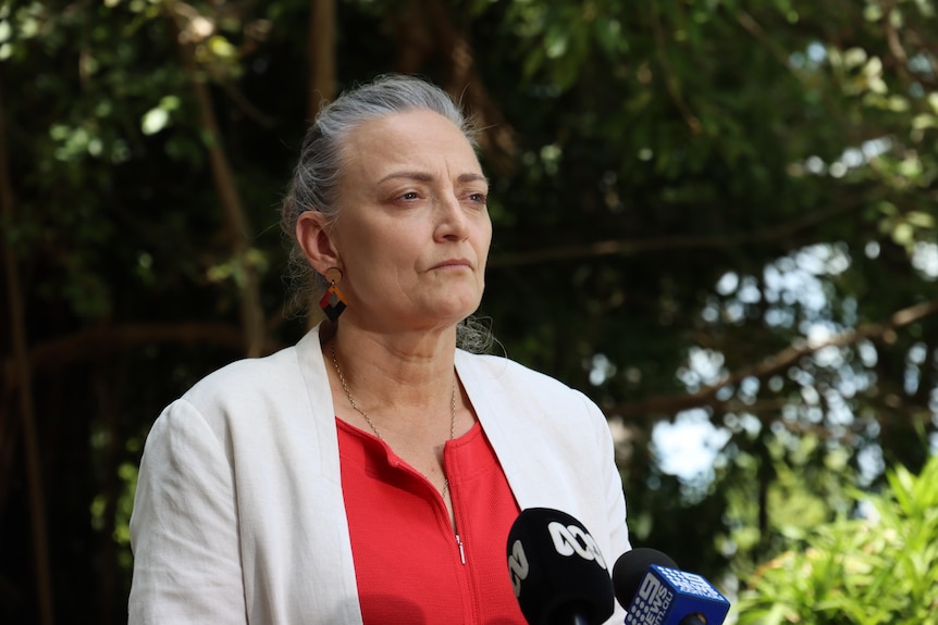 A woman with gray hair and a neutral expression looks out to the right of the camera