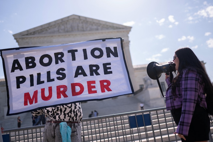 A woman shouts into a megaphone next to a sign that reads "Abortion pills are murder", outside the US Supreme Court