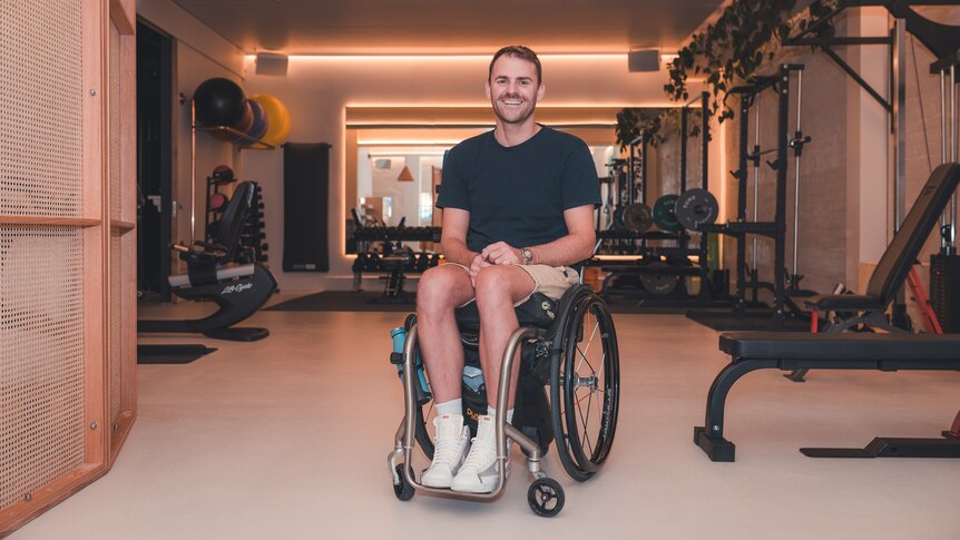 man in wheelchair smiling in a gym with equipment in background