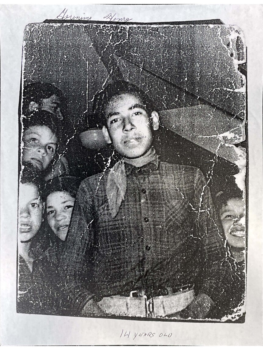 A black and white photo of a teenage boy, with other boys behind him