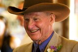 An older man in a cowboy hat and brown formal wear, smiling broadly.