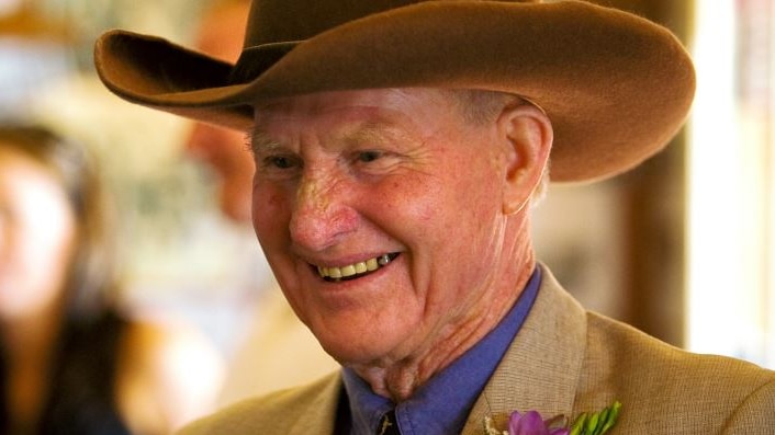 An older man in a cowboy hat and brown formal wear, smiling broadly.