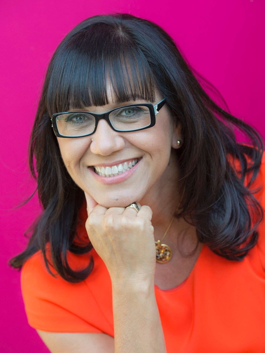 A woman with glasses and a big smile stands in front of a hot pink background.