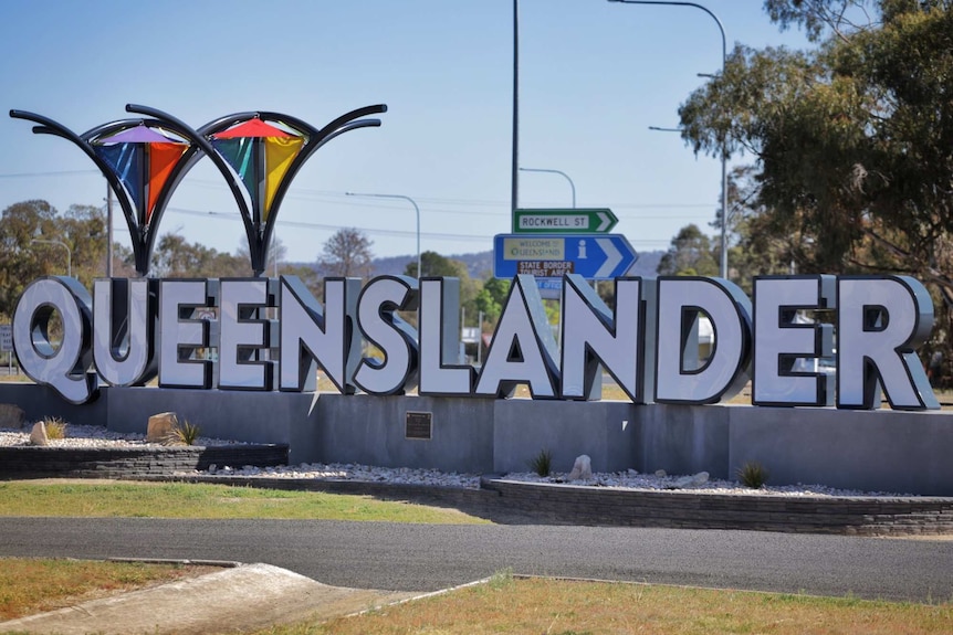 A large white sign of Queensland with individual white letters on concrete blocks in country town.