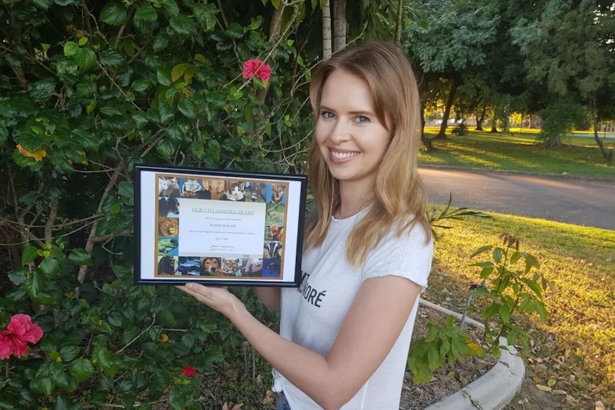 Elina walsh stands holding a framed Hero To Animals award from PETA Australia