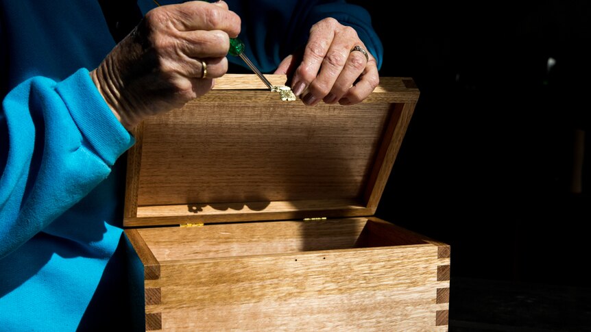 Hands screwing on a latch to a handcrafted baby coffin.