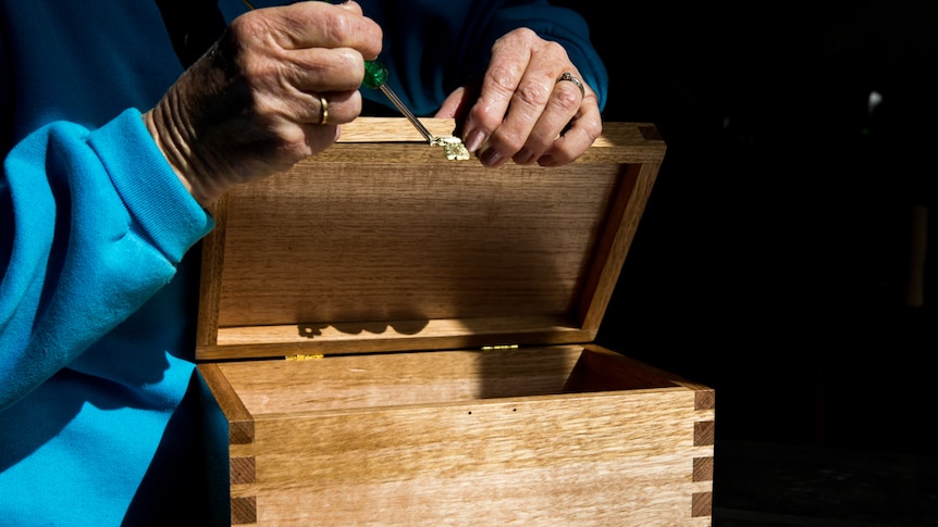 Hands screwing on a latch to a handcrafted baby coffin.