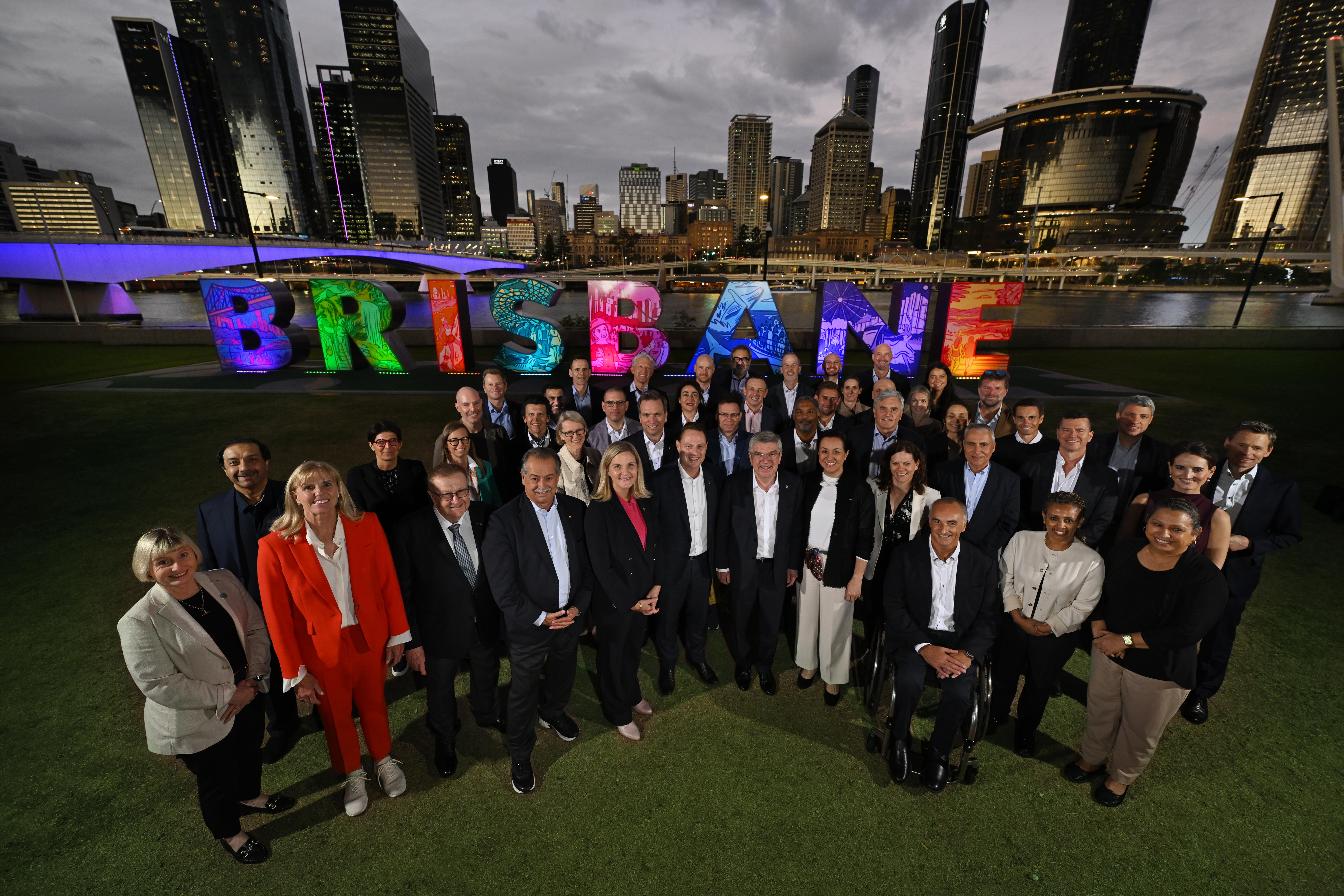 Membros do COI em frente a uma placa iluminada de BRISBANE 