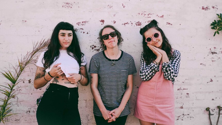 Camp Cope stand in front of a pink and red wall