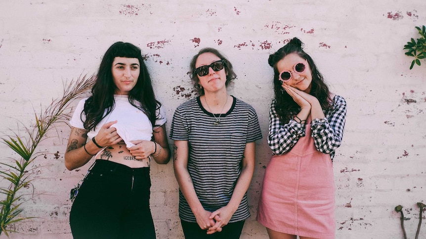 Camp Cope stand in front of a pink and red wall