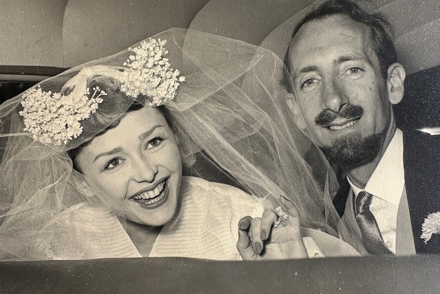 A woman smiles with a veil on next to a man in a suit.