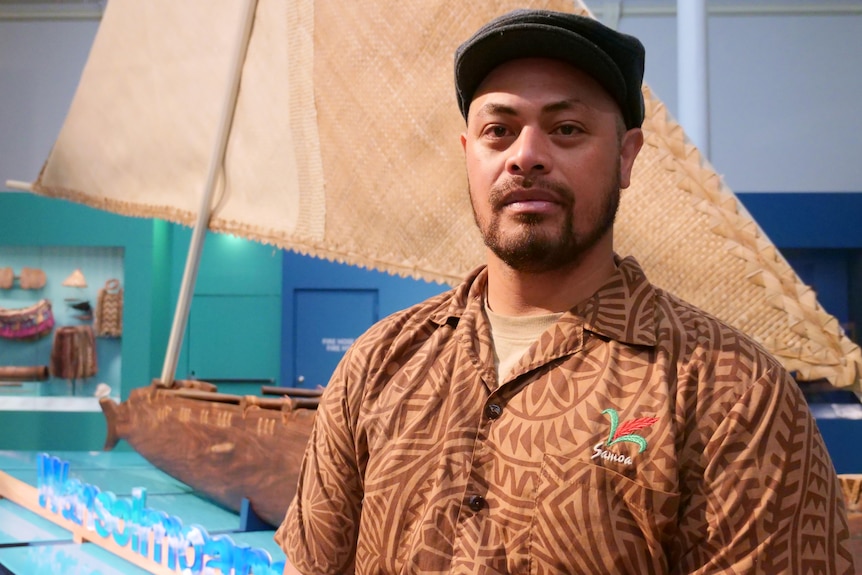 Samoan man Taofia Pelesasa wears a brown island design shirt and a beret hat, co-curator standing in front of the Tokelauan vaka