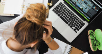 A young woman sits at a desk with her head in her hands.