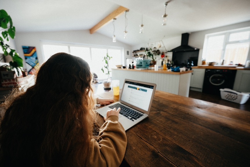 Young teenage girl working on a computer in a kitchen at home 