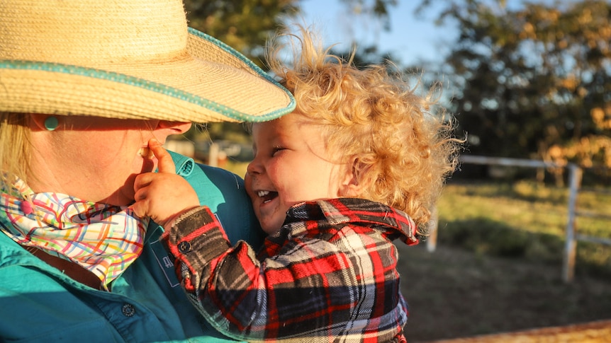 Laughing baby touches women's face surrounded by golden sunlight