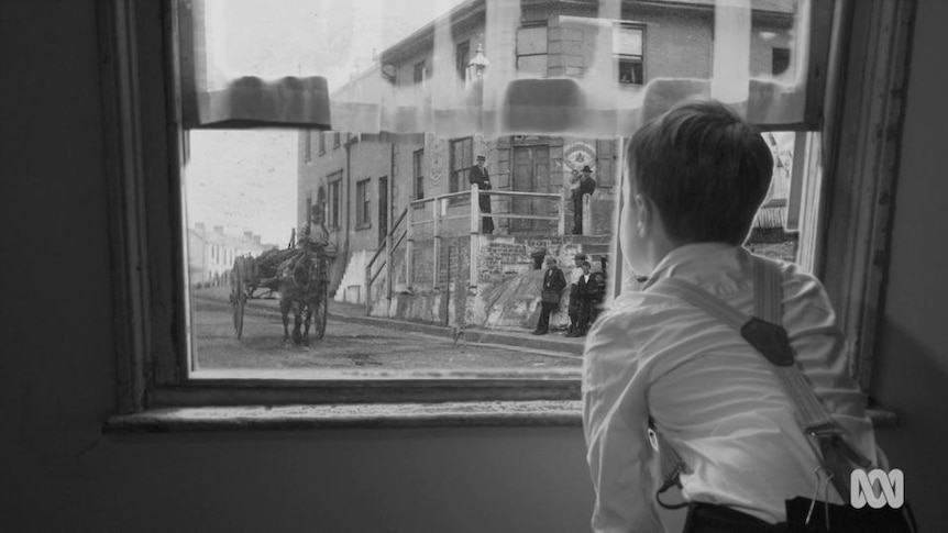 Old photo of boy looking out window into street