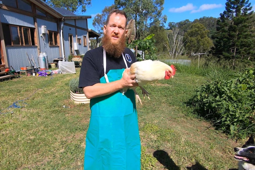 A bearded man holding a white chicken.