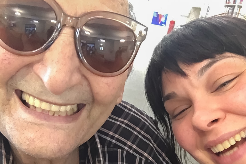 An older man wearing glasses smiling at the camera with his daughter next to him