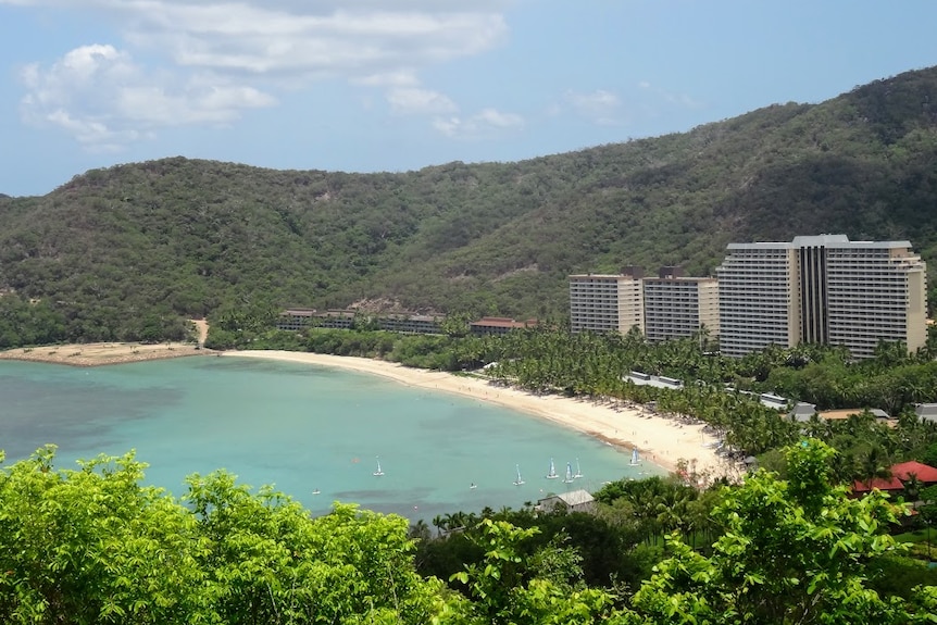 Looking out from a height over a beach, with buildings and mountains in the horizon. 