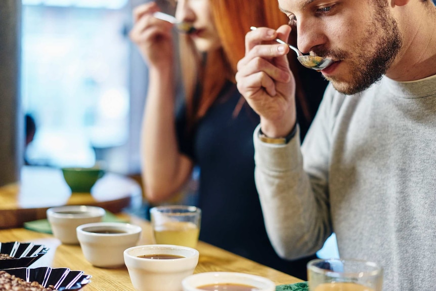 A man and a woman tasting coffee samples with different bowls of coffee beans in front of them