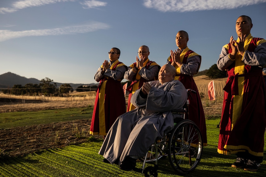 Master Wang sits in a wheelchair with four men dressed in religious robes standing behind him.