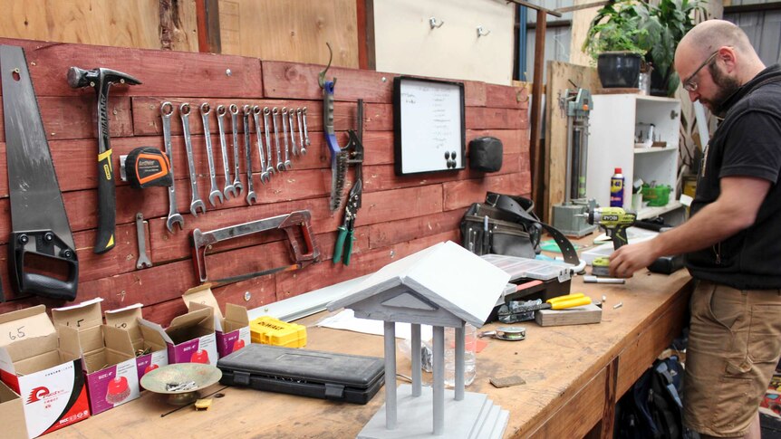 A man works on a bench surrounded by tools.